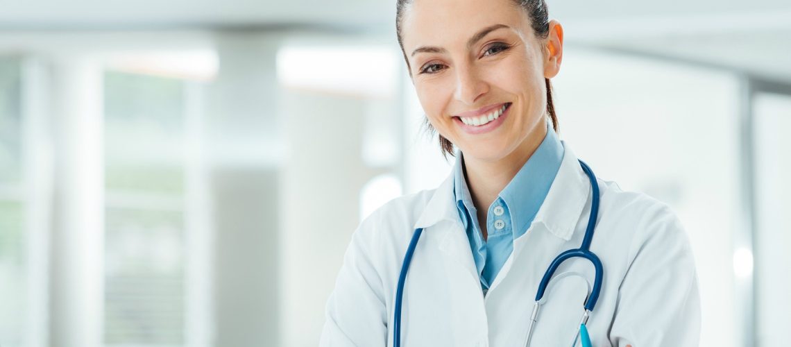 Confident female doctor sitting at office desk and smiling at camera, health care and prevention concept